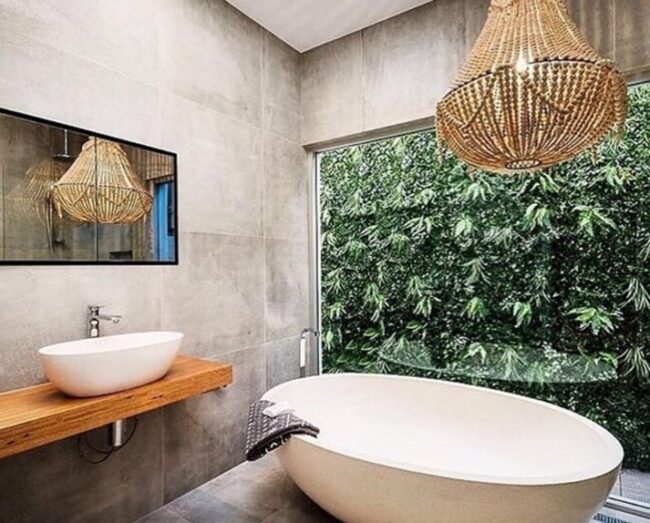 Image of a Pietra Bianca bath in a bathroom setting with a glass wall overlooking an outside garden hedge